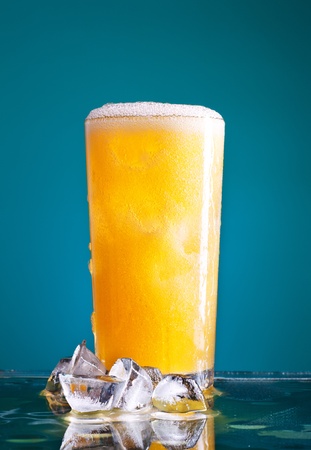 glass of orange soda with ice over blue backgroundの写真素材