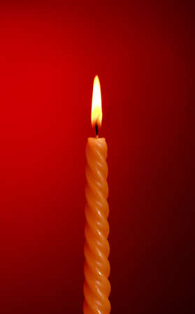 one twisted burning candle over red backgroundの写真素材