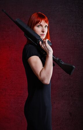 woman in black dress with sniper rifle, red backgroundの写真素材