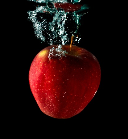 apple falling to water with splash over black backgroundの写真素材