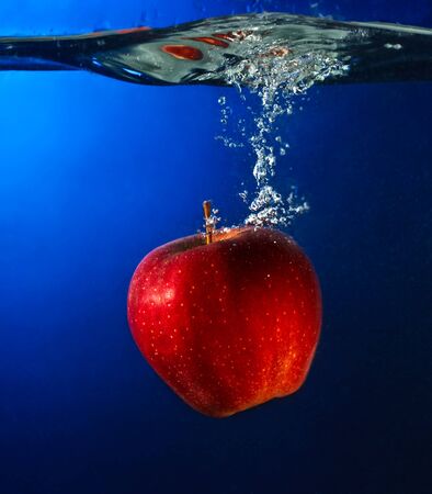 apple falling to water with splash over blue backgroundの写真素材