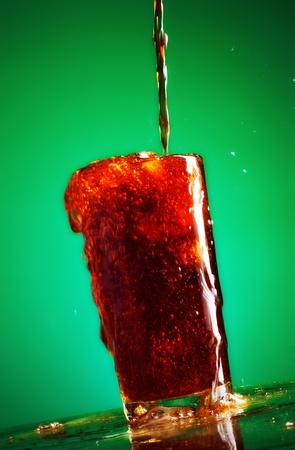 pouring cola in glass over green backgroundの写真素材