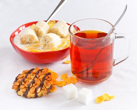 cornflakes with banana in bowl and tea with cookieの写真素材