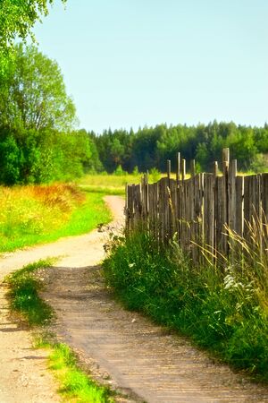 countryside road near old wooden fence at summer dayの写真素材