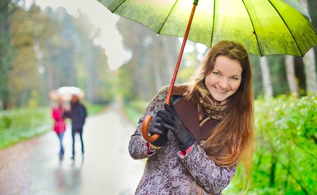 laughing girl and walking couple under rainfall in autumn parkの写真素材