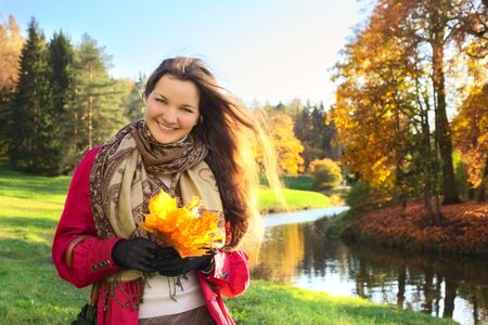 beautiful girl with bunch of maple leaves in autumn parkの写真素材