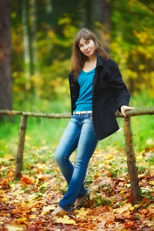 beautiful girl sitting on fence in autumn parkの写真素材