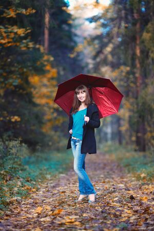beautiful girl with red umbrella standing in autumn parkの写真素材