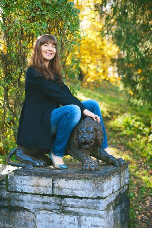beautiful girl saddle lion sculpture at autumn parkの写真素材
