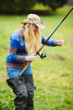 beautiful blond girl fishing in pond at autumnの写真素材