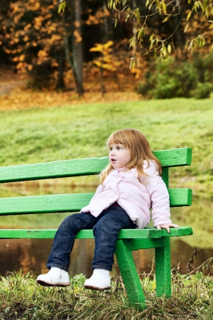 beautiful little girl on bench in autumn parkの写真素材