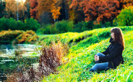 beautiful girl sitting on a shore in autumn forestの写真素材