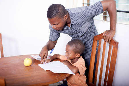 the housekeeper in a black shirt leaning over the schoolboy's shoulder trying to help him do his exercisesの写真素材