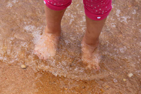 A close up view of clear water running over the toes of a small childの写真素材