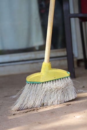 A Close up view of a yellow plastic broom with white bristles