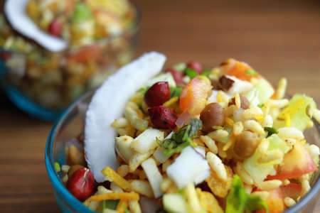Closeup of spicy puffed rice, popular Indian street food garnished with coconut slice, peanuts and...