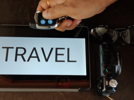 Picture of a car key, sunglasses and a  camera with travel written on a screen in background shot during daylight.の写真素材