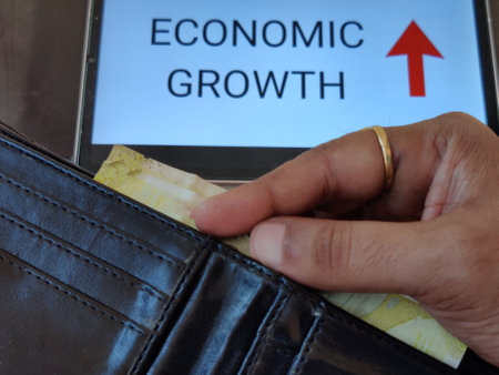 Picture of a person taking out money from his wallet. ECONOMIC GROWTH with an upward pointing arrow is written in background. Picture is depicting economic growth.の写真素材