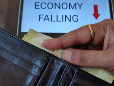 Picture of a person taking out money from his wallet. ECONOMY FALLING with a downward pointing arrow is written in background. Picture is depicting economic fall.の写真素材
