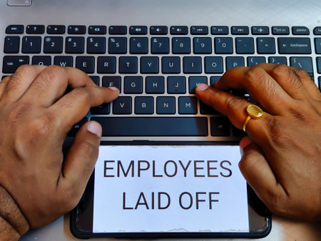 Picture of a person working on a laptop with EMPLOYEES LAID OFF on a screenの写真素材