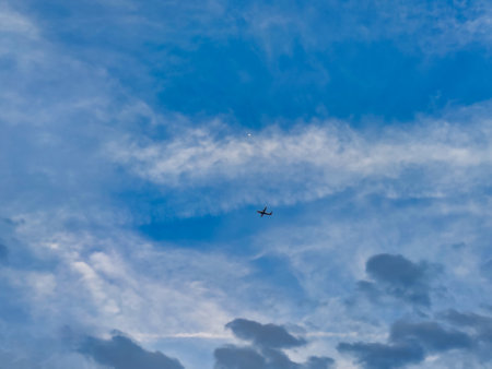 Picture of white clouds in blue sky shot during daylight on a cloudy day. An airplane flying can also be seen.の写真素材