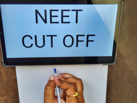 Picture of a person writing on a paper with a pen with NEET CUT OFF written on a screen. NEET is a medical entrance exam in India in which many candidates appear every year.の写真素材