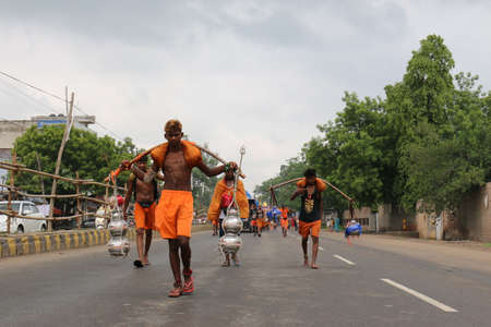 GHAZIABAD, UTTAR PRADESH, INDIA - JULY 2019: A hindu devotee carrying kanwar on their shoulder to perform the yearly kanwar yatra with holy Ganga water walking on streets barefoot.のeditorial素材