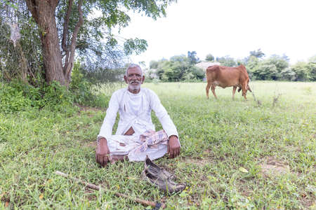 Jawai, Rajasthan, India - September 2021: Portrait of a male shepherd of the Rabari ethnic group in a national headdress and traditional white dress and red turban on the field of Jawai.のeditorial素材