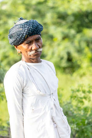Jawai, Rajasthan, India - September 2021: Portrait of a male shepherd of the Rabari ethnic group in a national headdress and traditional white dress and red turban on the field of Jawai.のeditorial素材