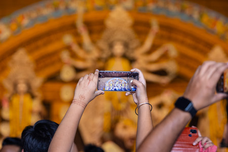 Hand holding mobile phone and taking photos of Goddess Durga idol at a pandal. Durga Puja is the biggest religious festival of hindus of Bengali Community.の写真素材