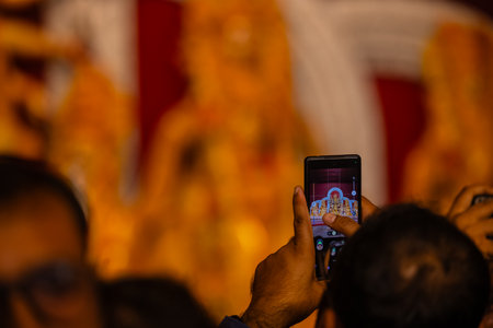 Hand holding mobile phone and taking photos of Goddess Durga idol at a pandal. Durga Puja is the...