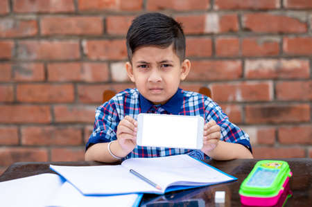 Primary school student in proper school uniform reading book on study table in classroom. Indian...