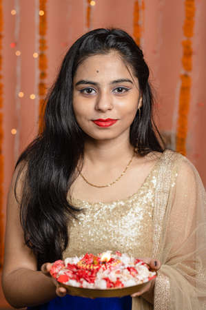 Beautiful Young Indian woman holding burning Diya and looking at camera. Diwali or deepawali celebration with light bokeh in background.の写真素材