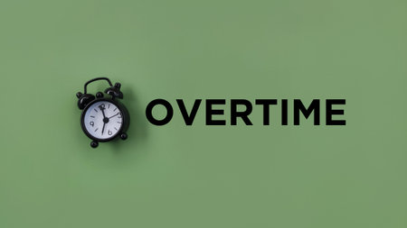 Conceptual black alarm clock with text OVERTIME ongreen backgroundの写真素材