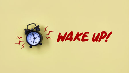 Conceptual black alarm clock with text WAKE UP on yellow backgroundの写真素材