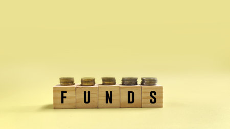 stacked coins with FUNDS words on wooden blocks on yellow background. Funding and business conceptの写真素材