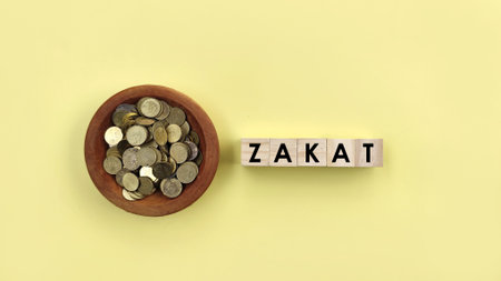 Top view coins in wooden bowl with ZAKAT words on yellow background. Islamic donation conceptの写真素材