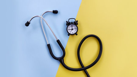 Minimalist medical appointment concept with a stethoscope and alarm clock on a blue and yellow background. Suitable for medical communication, organization and appointment reminderの写真素材