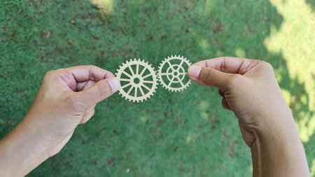 Hands holding wooden gear wheels outdoors, representing teamwork, system, collaboration, mechanics, and business process concept.の写真素材