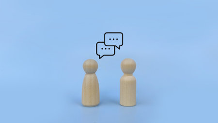 Two wooden peg figures facing each other with speech bubbles, symbolizing conversation, dialogue, communication and relationship concept on minimal blue background.の写真素材