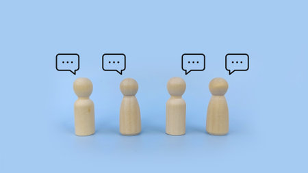 Group of wooden peg figures standing in a row with speech bubbles, representing group discussion,...