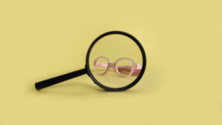Children glasses seen through magnifying glass on yellow background. Visual concept of focus, examination, and supportive child vision care with inclusive eyewear design.の写真素材