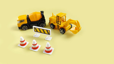 Mini toy cement truck and excavator with traffic barriers and cones representing roadwork,...