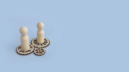Two wooden figures standing on gears representing collaboration, teamwork, and moving business...
