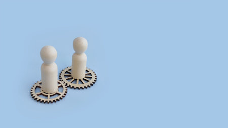 Two wooden figures on gear wheels symbolizing partnership, teamwork, and cooperation in business.
