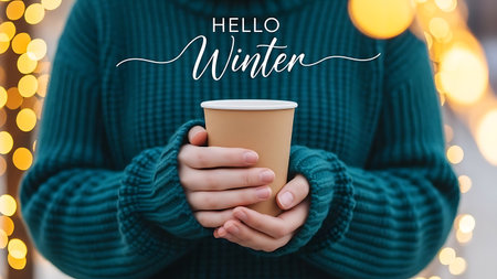 Female hands holding paper cup of hot drink with Hello Winter lettering on background bokeh lightsの素材