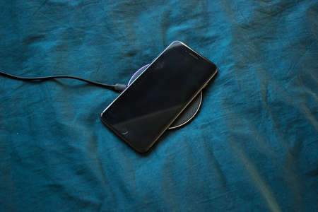 Black mobile phone is charging on the black round shape wireless charger isolated on blue background.の写真素材