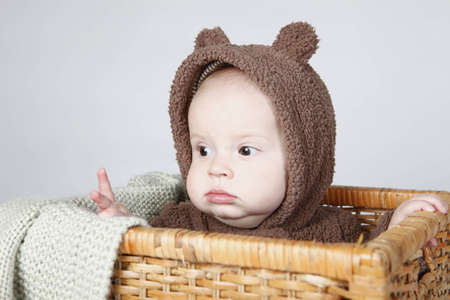 Baby boy sitting in a basket wearing a fully bear suit の写真素材