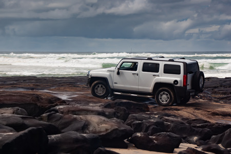 A 4wd Hummer negotiating rocks on a rocky beach on a stormy dayの写真素材