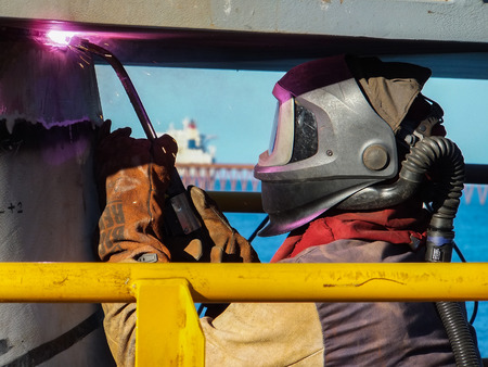 A welder with all of the correct protective equipment safely welds a wharf headstock to a pile